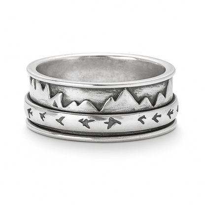 Silver spinner ring with engraved mountains and flying birds, dual-band rotating design, photographed on a white background with a soft shadow